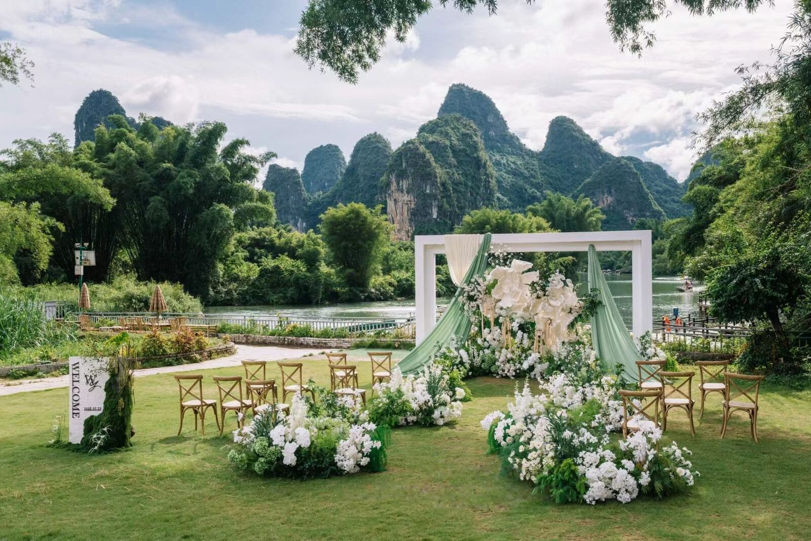 A riverside ceremony lawn with a white arch, the Li River and karst peaks behind