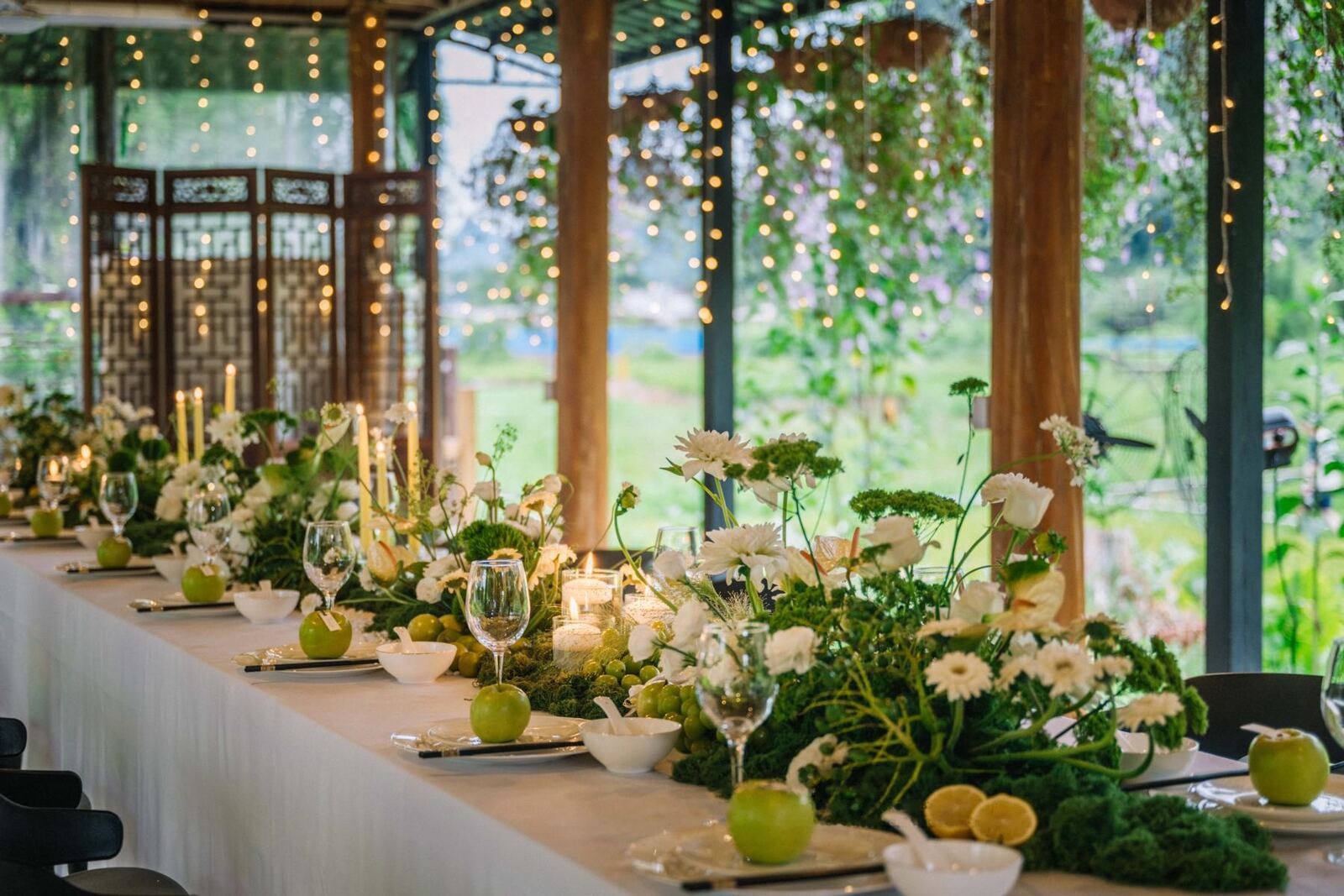 A long banquet table dressed in greenery and candles under a timber pavilion