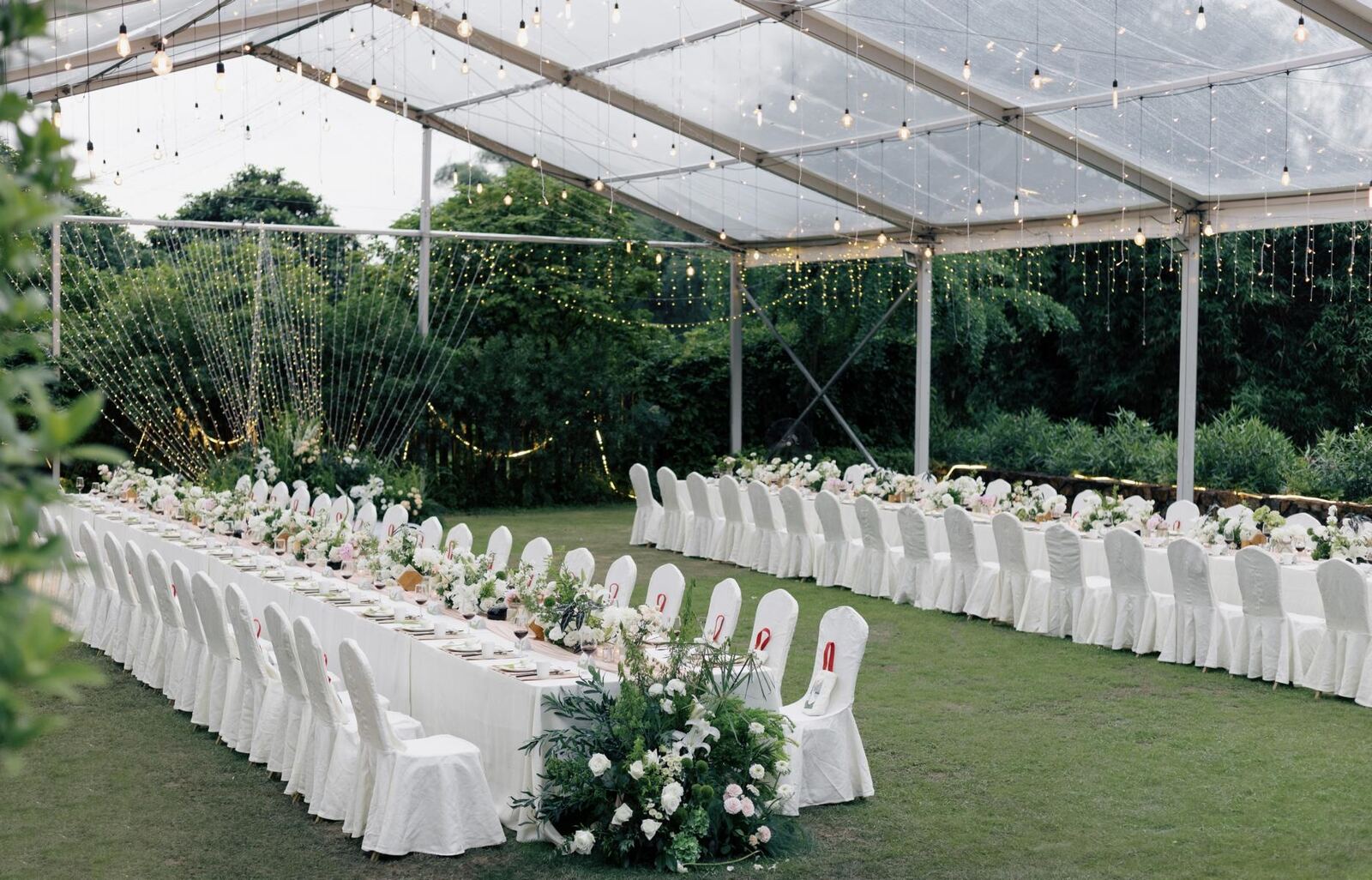 A long banquet laid under a clear marquee on a lawn, a covered alternative to dining in the open