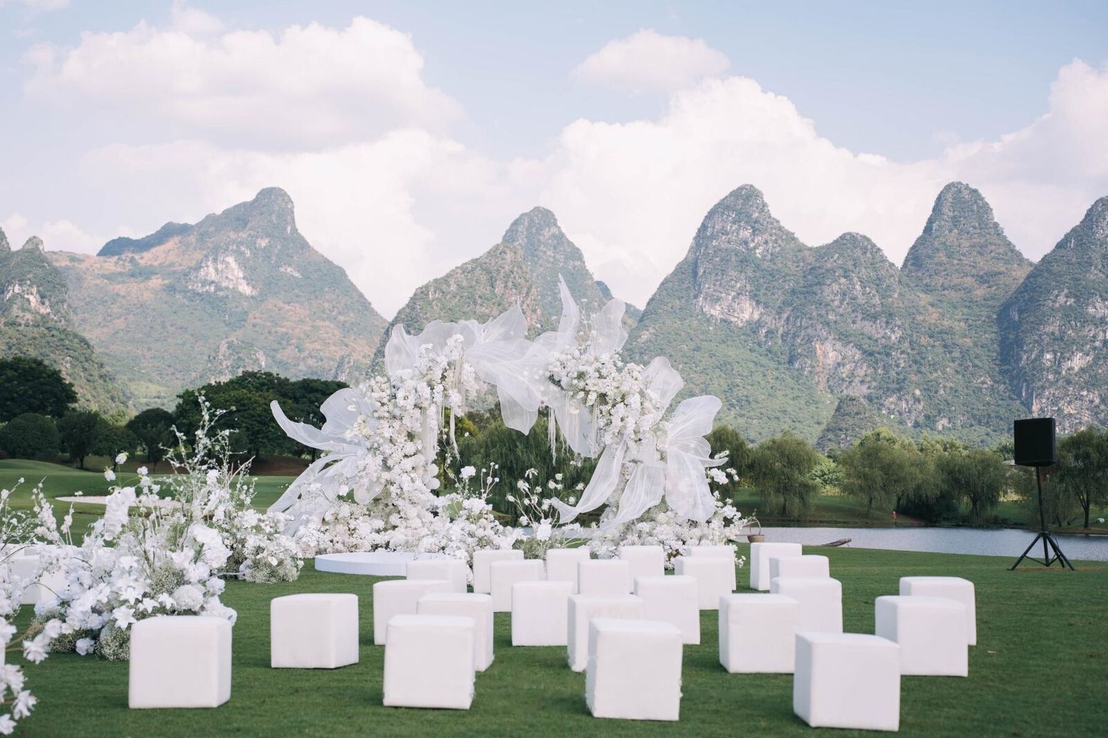 A white floral ceremony arch on open grass below a ridge of karst peaks