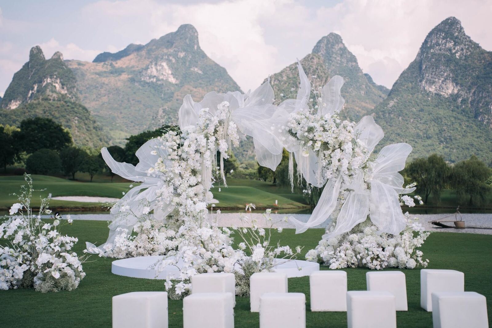 An open-air white floral ceremony build in front of karst mountains