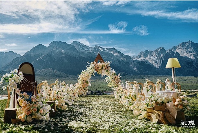 A white floral ceremony arch on an alpine meadow beneath the Yulong range near Lijiang
